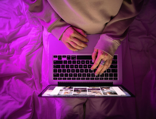 Woman-Using-Laptop-In-Bed-Pink-Lighting-