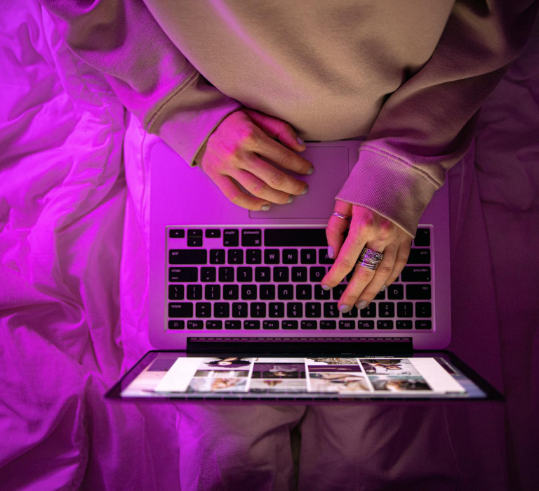 Woman using laptop in bed with pink lighting